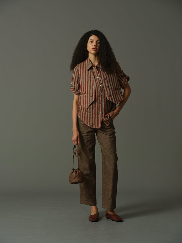 Woman wearing a striped shirt and brown pants holding a bag against a gray background