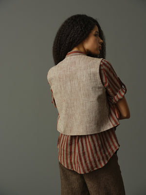Woman wearing a striped shirt and vest against a gray background