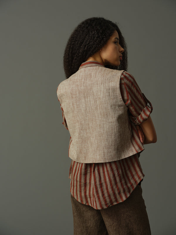 Woman wearing a striped shirt and vest against a gray background