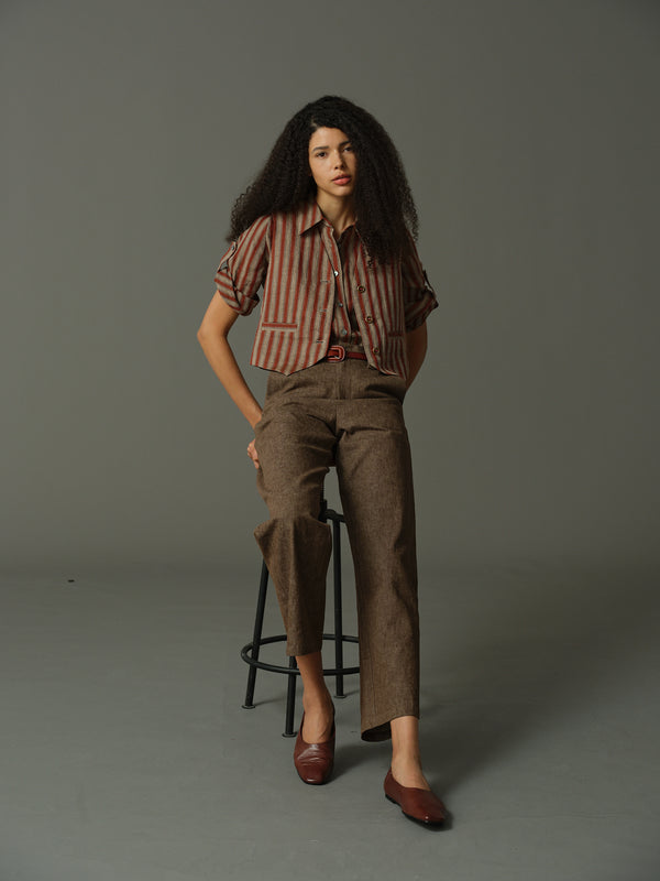 Woman in a striped shirt and brown pants standing on a stool against a gray background