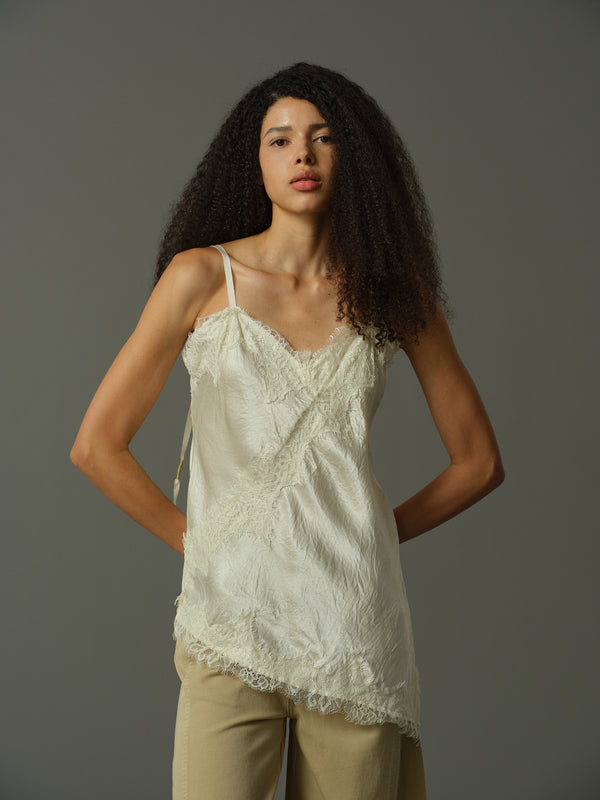 Woman wearing a ivory lace top and beige pants against a gray background