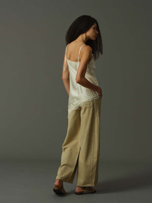 Woman wearing a light-colored lace top and beige pants against a gray background