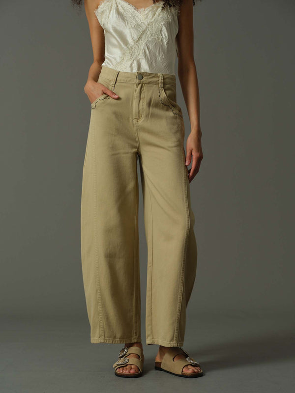 Person wearing beige high-waisted pants and a white top against a gray background