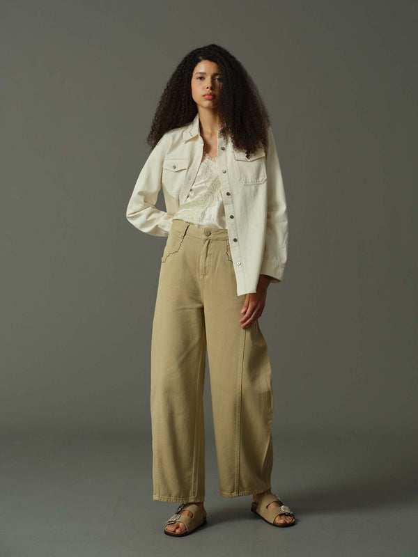 Woman wearing a white shirt and beige pants against a gray background