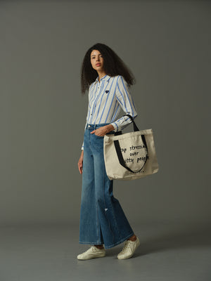 Woman holding a tote bag with quote, wearing a striped shirt and jeans, on a gray background