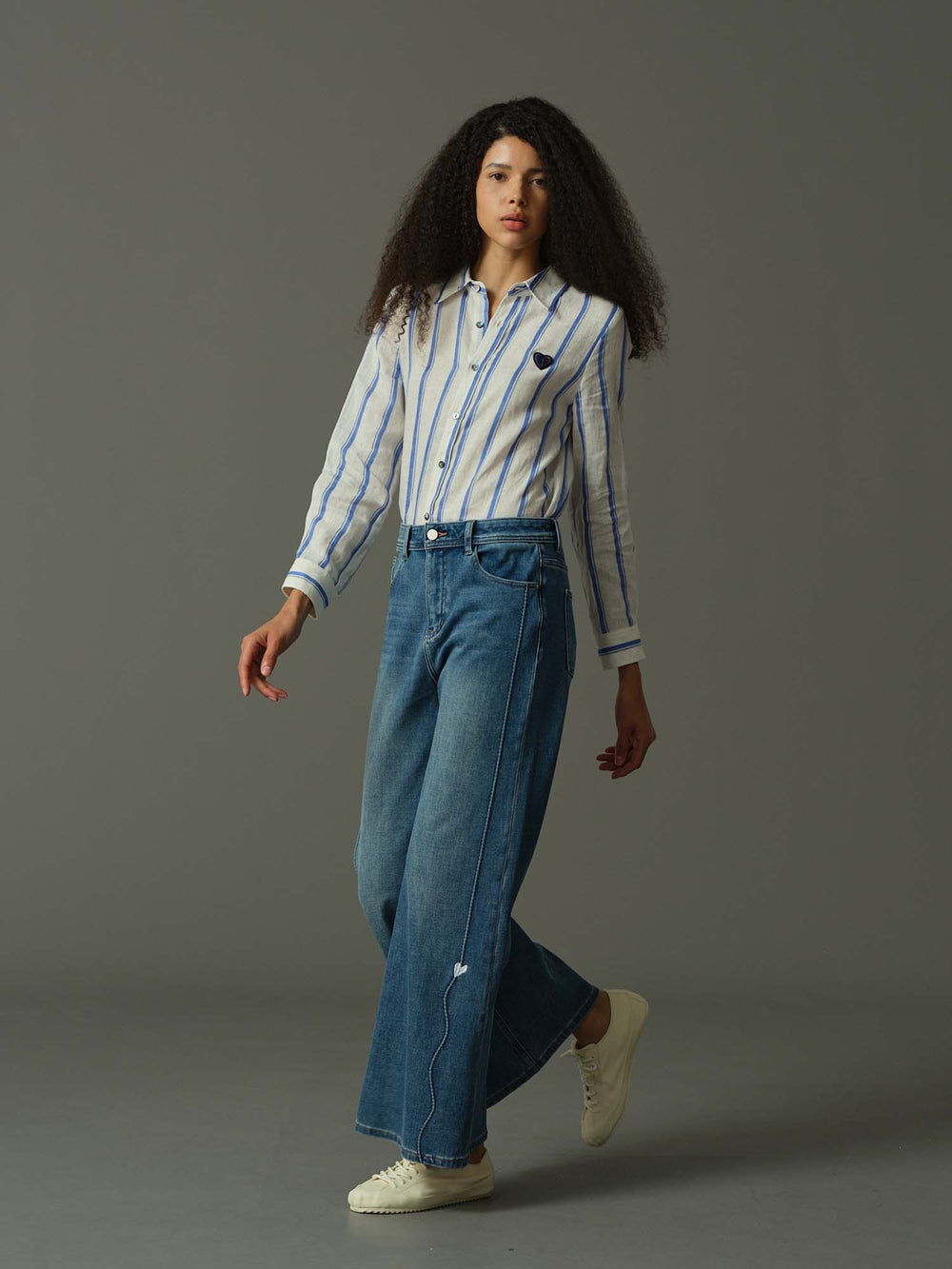 Woman wearing a striped shirt and blue jeans on a gray background