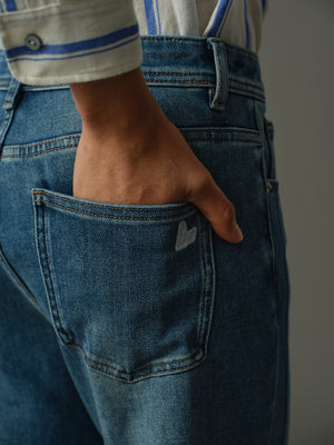 Person wearing blue jeans with a heart design on pocket on a plain background
