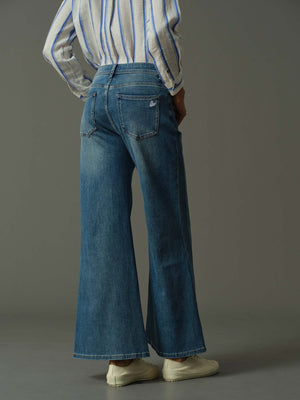 Person wearing blue flared jeans with white heart embroidery and a striped shirt on a gray background