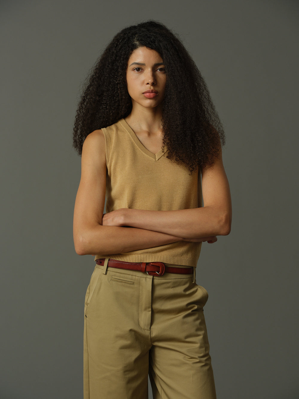 Woman wearing a beige sleeveless sweater against a gray background