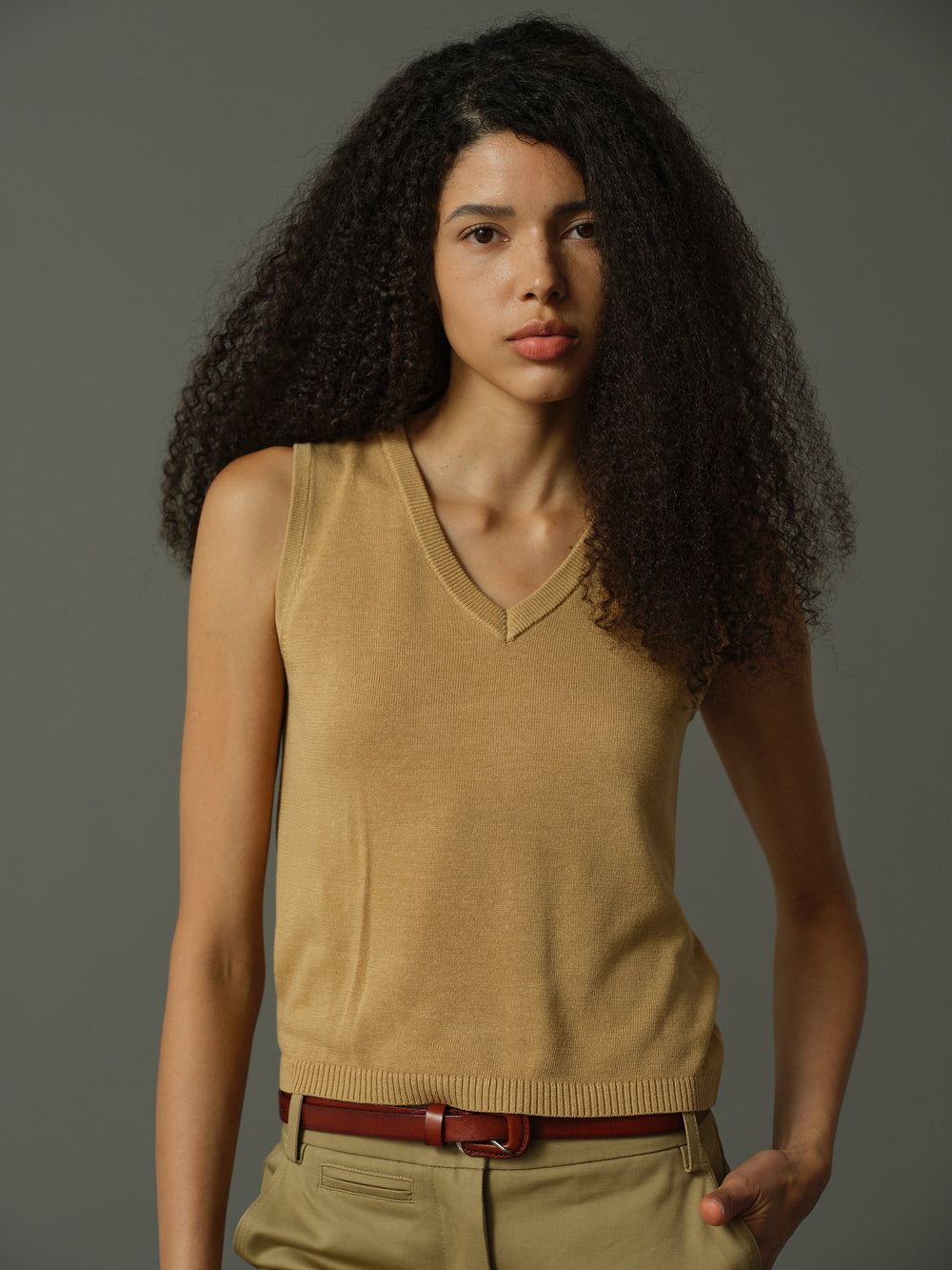 Woman wearing a beige sleeveless sweater against a gray background