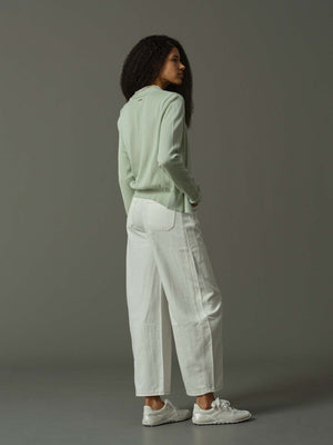 Person wearing a light green jacket and white pants against a gray background