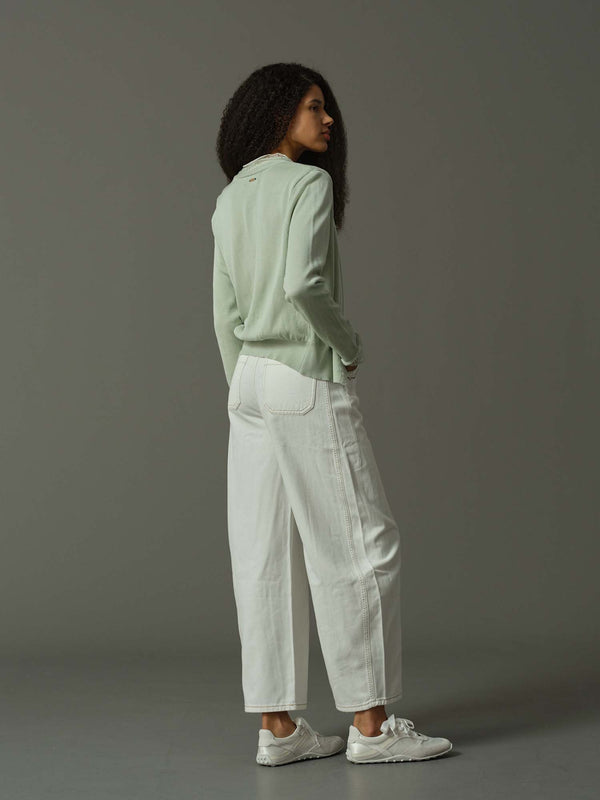 Person wearing a light green jacket and white pants against a gray background