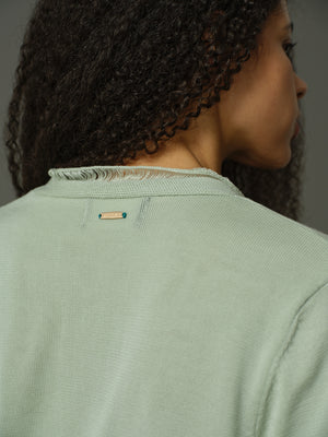 Person wearing a light green shirt with a brand logo on the collar.