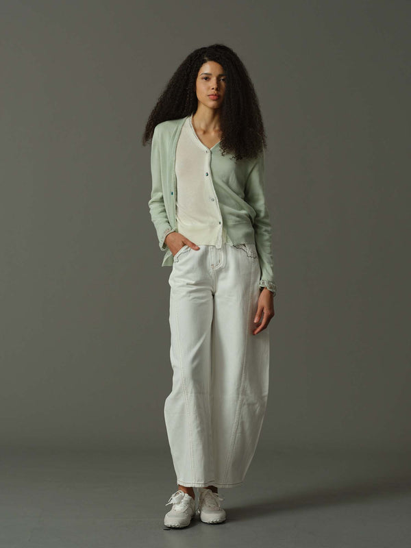 Woman wearing a light green cardigan, white shirt, and white pants against a gray background