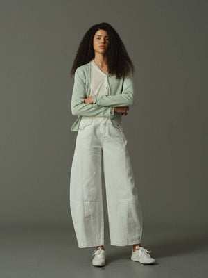 Woman wearing a light green cardigan and white pants against a gray background