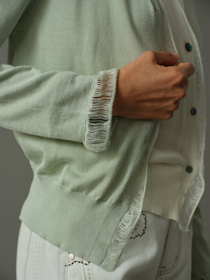 Light green cardigan with white trim worn by a person, with a neutral background