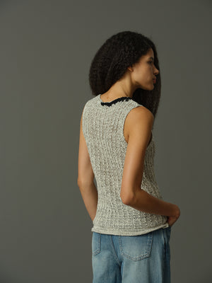 Woman wearing a textured sleeveless top and blue pants against a gray background