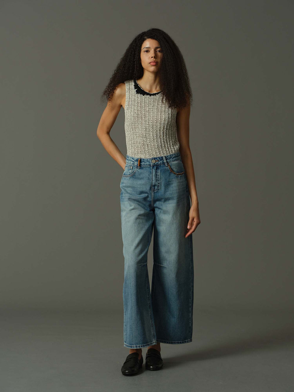 Woman wearing a sleeveless patterned top and blue jeans against a gray background