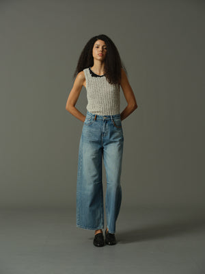 Woman wearing a sleeveless top and jeans against a gray background