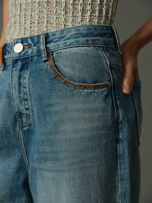 Close-up of blue jeans with orange decorative stitch along the pocket with a blurred background