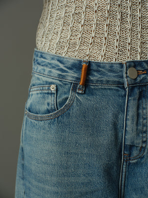 Close-up of blue jeans with orange decorative stitch a patterned sweater on a gray background