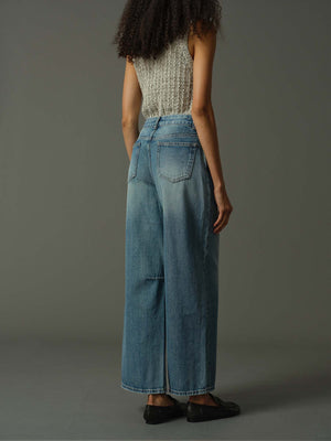 Person wearing a sleeveless top and wide-leg jeans against a gray background