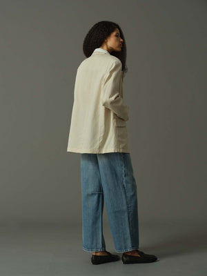 Person wearing a beige jacket and blue jeans against a gray background