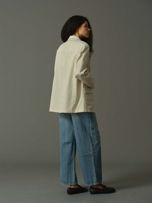 Person wearing a beige jacket and blue jeans against a gray background