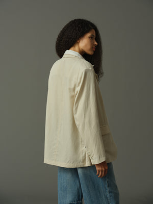 Person wearing a beige jacket and blue jeans against a gray background