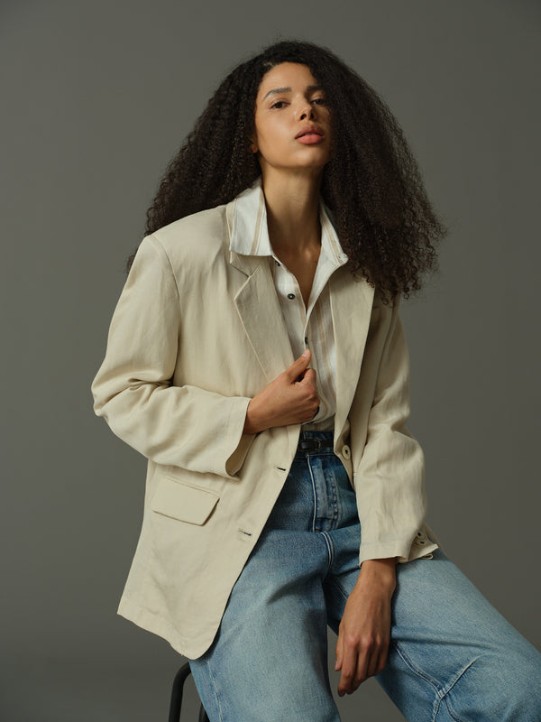 Woman wearing a beige jacket and blue jeans against a gray background