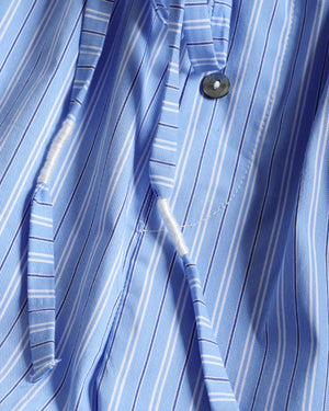 Close-up of a blue and white striped dress shirt fabric, showing the collar, button, and a loose white thread near the placket.