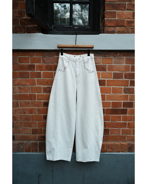 White wide-leg jeans hanging on a wooden hanger against a brick wall.