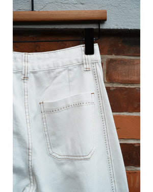 Light-colored pants hanging on a wooden rack against a brick wall.