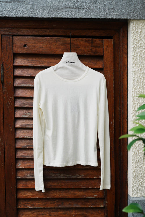 White long-sleeve shirt on a wooden surface with a light gray wall and green leaves in the background