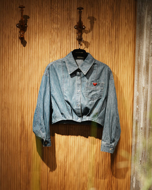 cropped denim jacket with heart embroidery on chest pocket, hanging on a brown textured wall