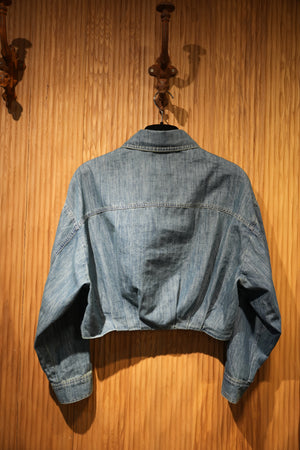 back of a cropped denim jacket with heart embroidery on chest pocket, hanging on a brown textured wall