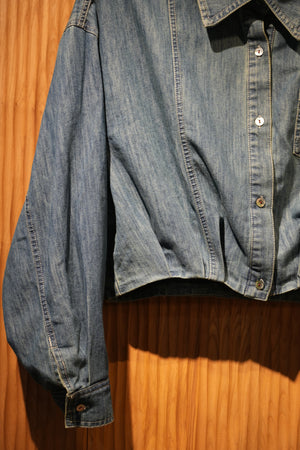 close up of a denim jacket with heart embroidery on chest pocket, hanging on a brown textured wall