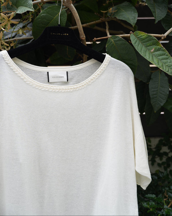 close up of a white top with braided neckline hanging on the tree