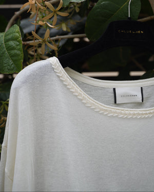 close up of a white top with braided neckline hanging on the tree