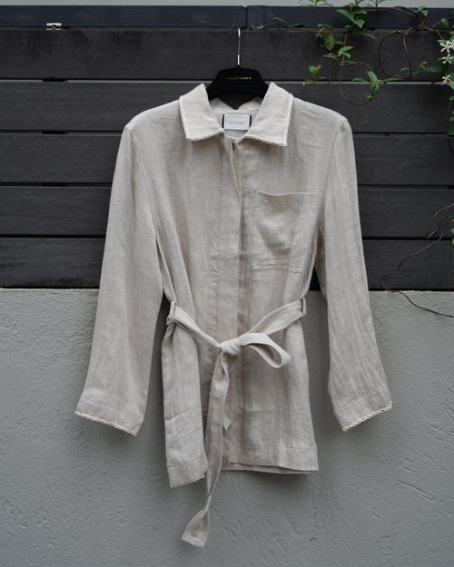 Light-colored jacket with a belt on a dark wooden surface against a gray wall.