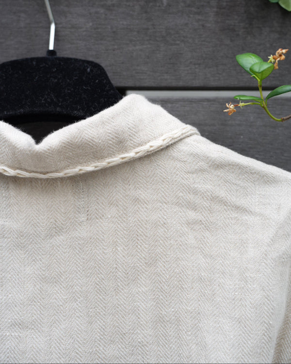 Close-up of a back of the linen jacket against a dark background with a plant.