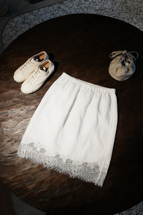 White lace skirt on a wooden surface with white sneakers and a beige bag.