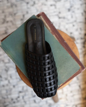 Black woven leather flats on a book with a marble surface