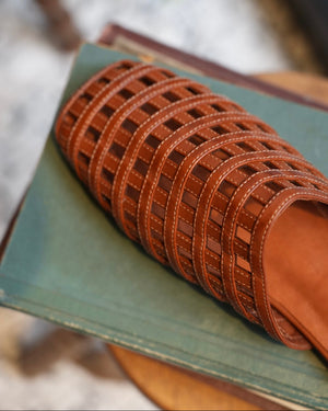 Brown sandal with woven design on a green surface