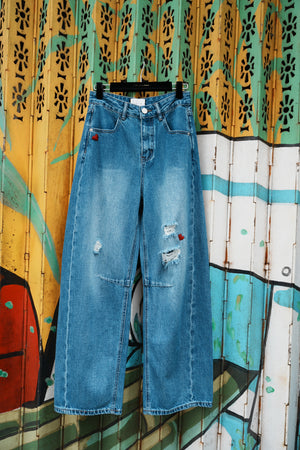 Blue jeans on a hanger against a colorful, abstract wall.