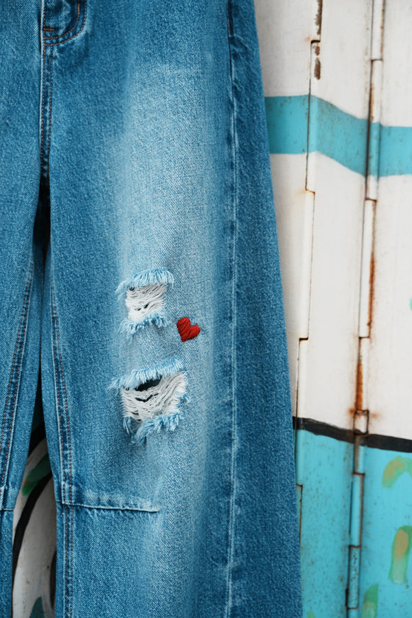 Ripped blue jeans with a red heart patch on a wooden surface
