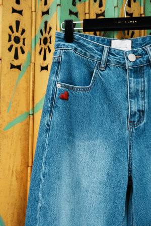 Close-up of blue jeans with a red heart button on a decorative surface