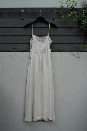 back of a beige dress on a mannequin against a gray wall with a black floor.
