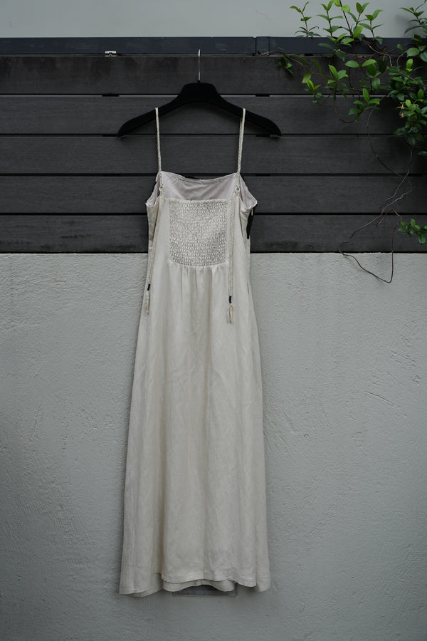 back of a beige dress on a mannequin against a gray wall with a black floor.