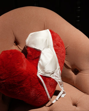 White bra on a red heart shaped cushion against a pink sofa